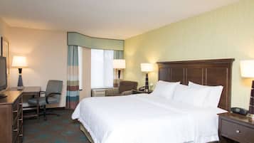 A hotel room with a large bed, a desk with a chair, a television, and two lamps.