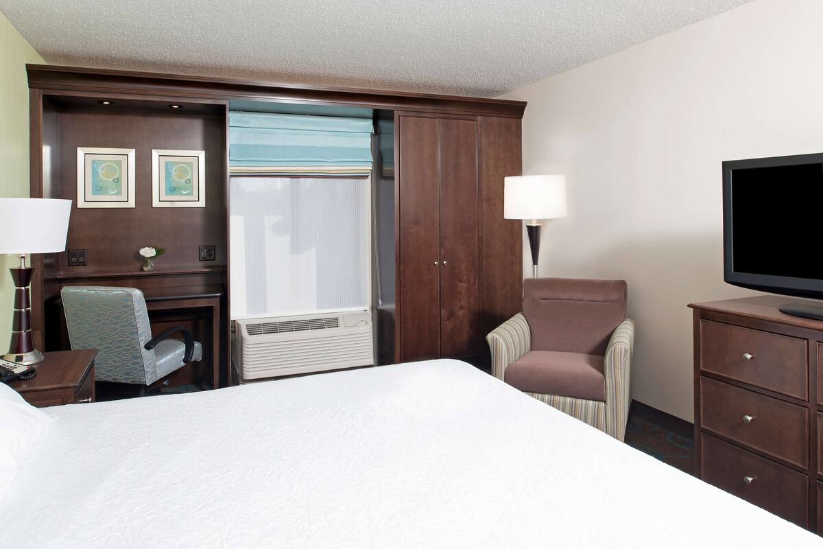 A hotel room with a bed, a desk, a chair, a TV, and a wardrobe.