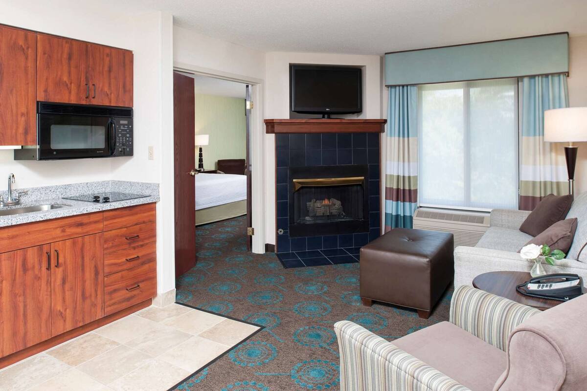 A hotel room with a kitchenette, a fireplace, a TV, a sofa, and a bed.
