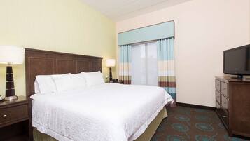 Una habitación de hotel con una cama grande, dos mesitas de noche con lámparas, un televisor sobre un mueble y una ventana con cortinas.