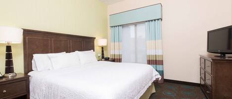 A hotel room with a large bed, two bedside tables with lamps, a television on a cabinet, and a window with curtains.