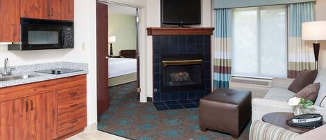 A hotel room with a kitchenette, a fireplace, a television, a sofa, and a bed.