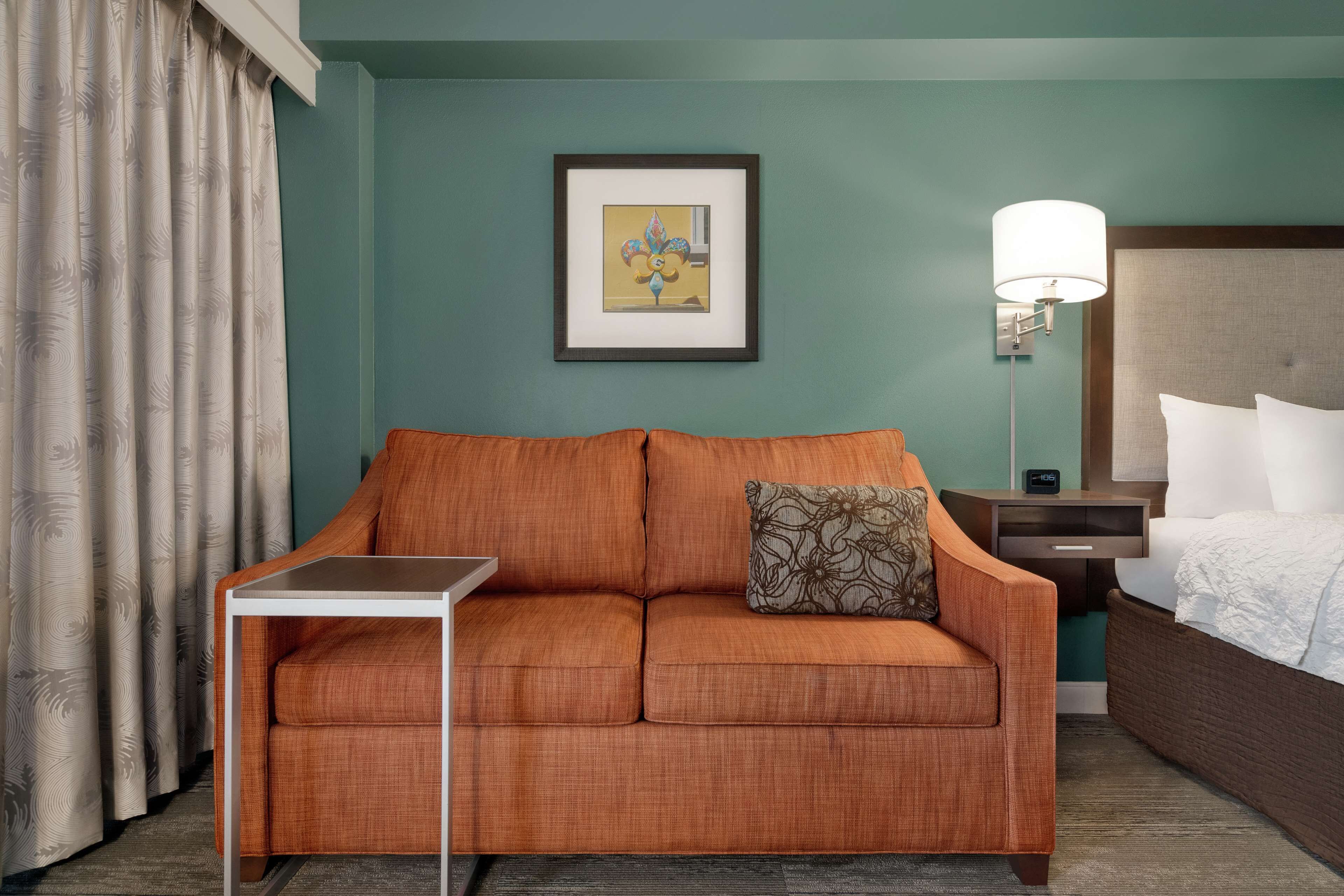 Habitación de hotel con sofá, una mesita, cama, mesita de noche, lámpara y un cuadro en la pared.