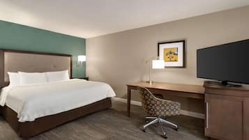 Habitación de hotel con cama, escritorio, silla, televisor y una obra de arte en la pared.