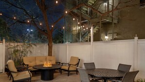 Un patio al aire libre con una mesa redonda, sillas, una chimenea y luces colgantes.
