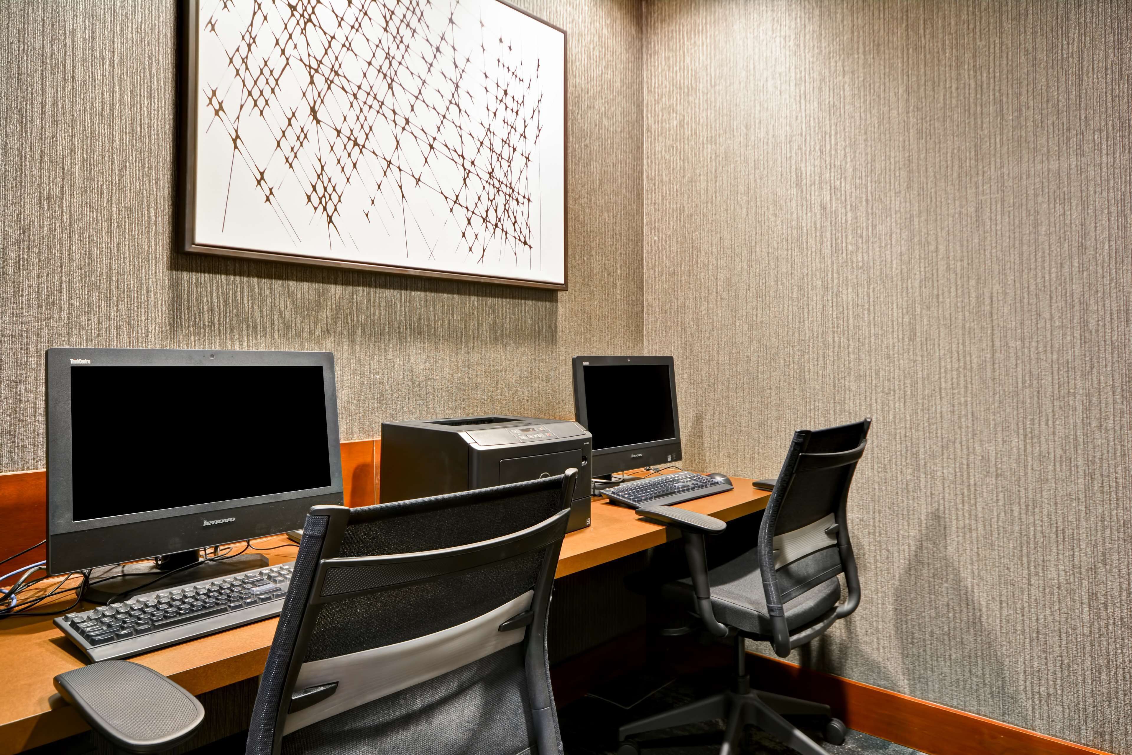 A workspace with two monitors, a keyboard, and a printer on a wooden desk.