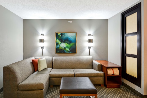 A modern hotel room with a sectional sofa, a small wooden table, and two wall-mounted reading lamps.