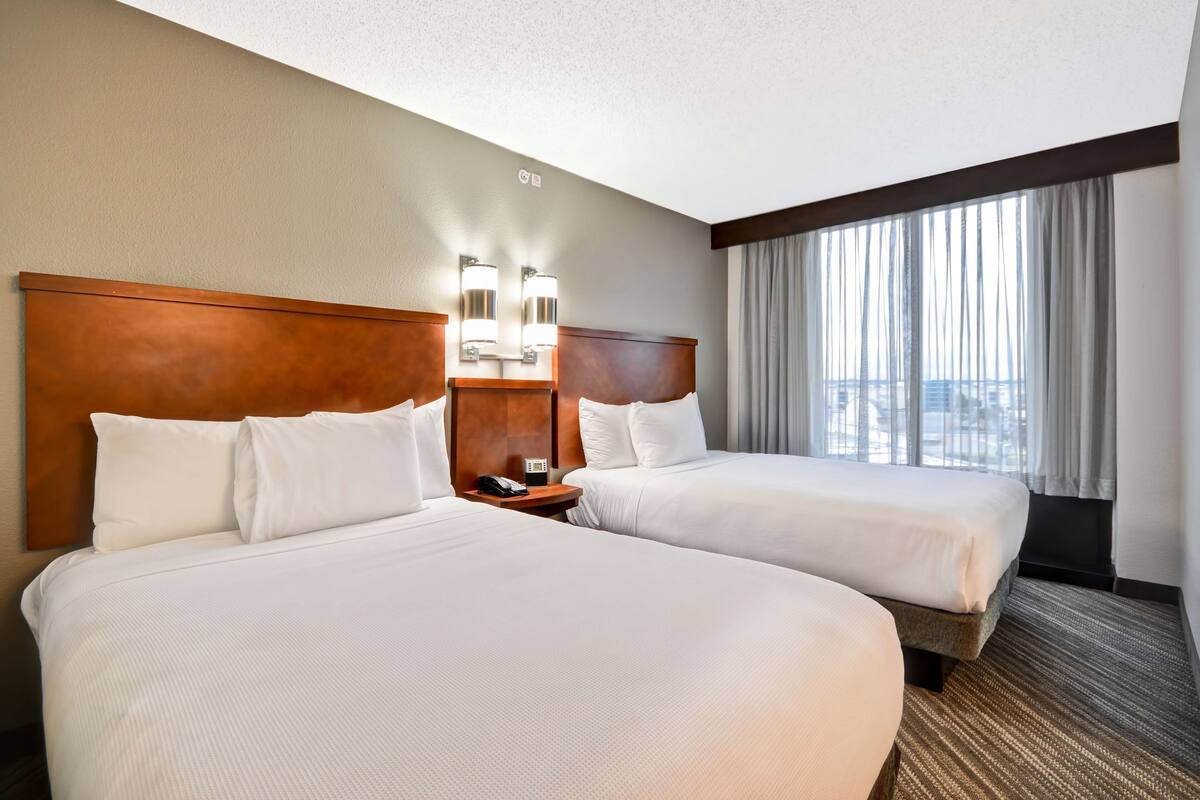 A hotel room with two beds, a wooden headboard, a nightstand with a phone, and a window with curtains.