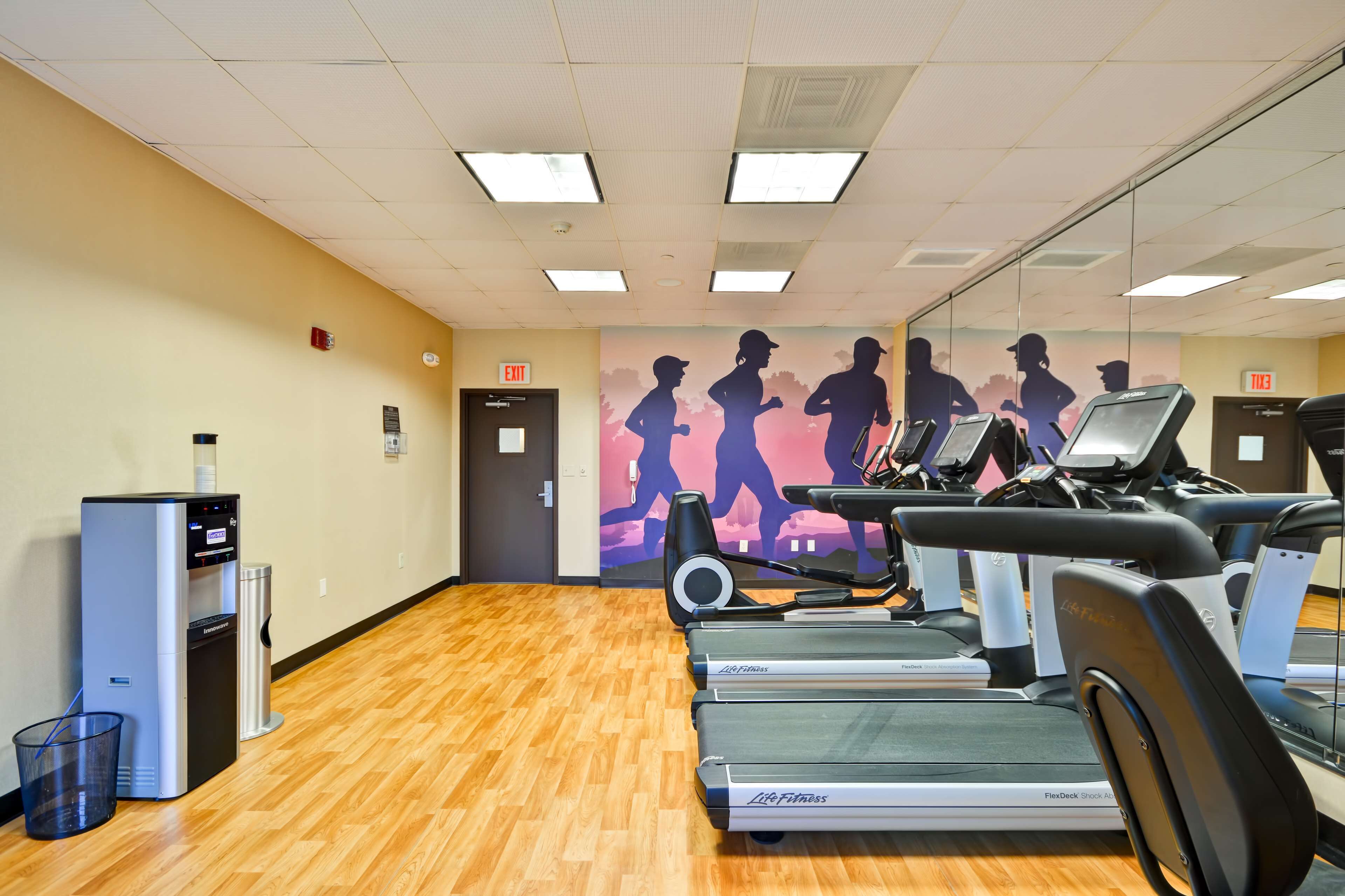 A gym with treadmills, a water dispenser, and a mirror wall with silhouettes of runners.