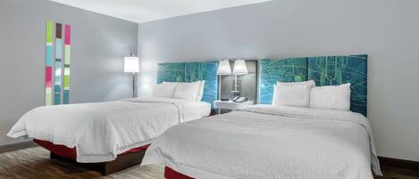 A hotel room with two beds, a modern headboard, a bedside table with a lamp, and a colorful abstract wall decoration.