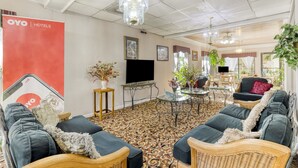 A hotel lobby with a patterned carpet, wicker furniture, a TV, and a red OYO Hotels banner.