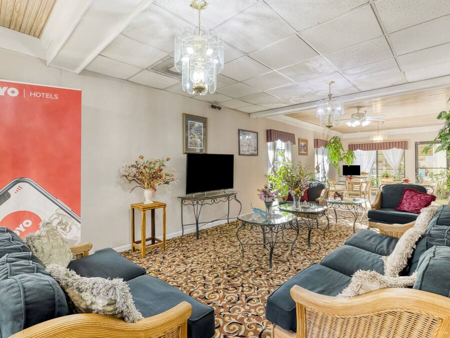 A hotel lobby with a patterned carpet, wicker furniture, a TV, and a red OYO Hotels banner.