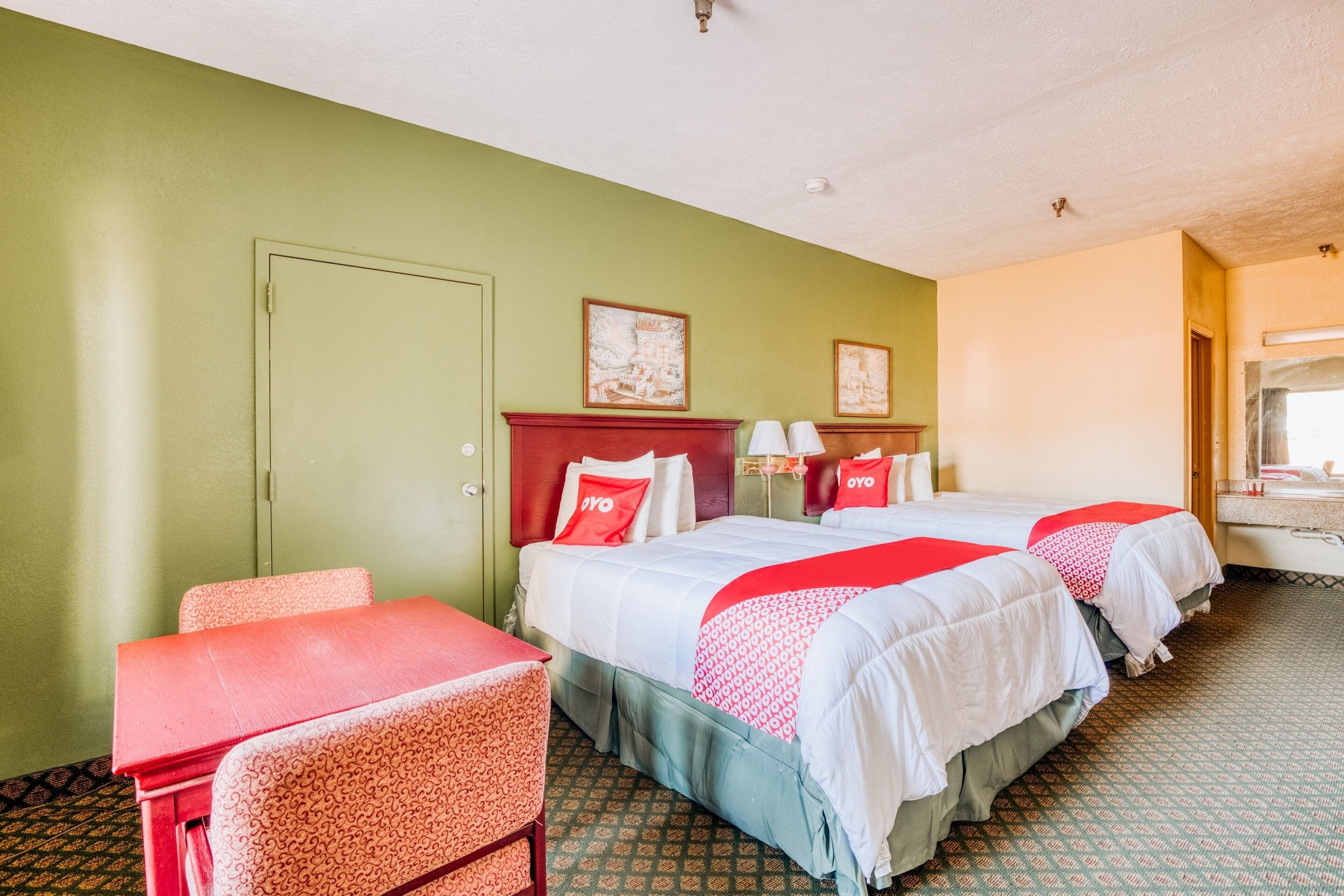 A hotel room with two beds, a desk, a chair, and a bathroom visible through an open door.