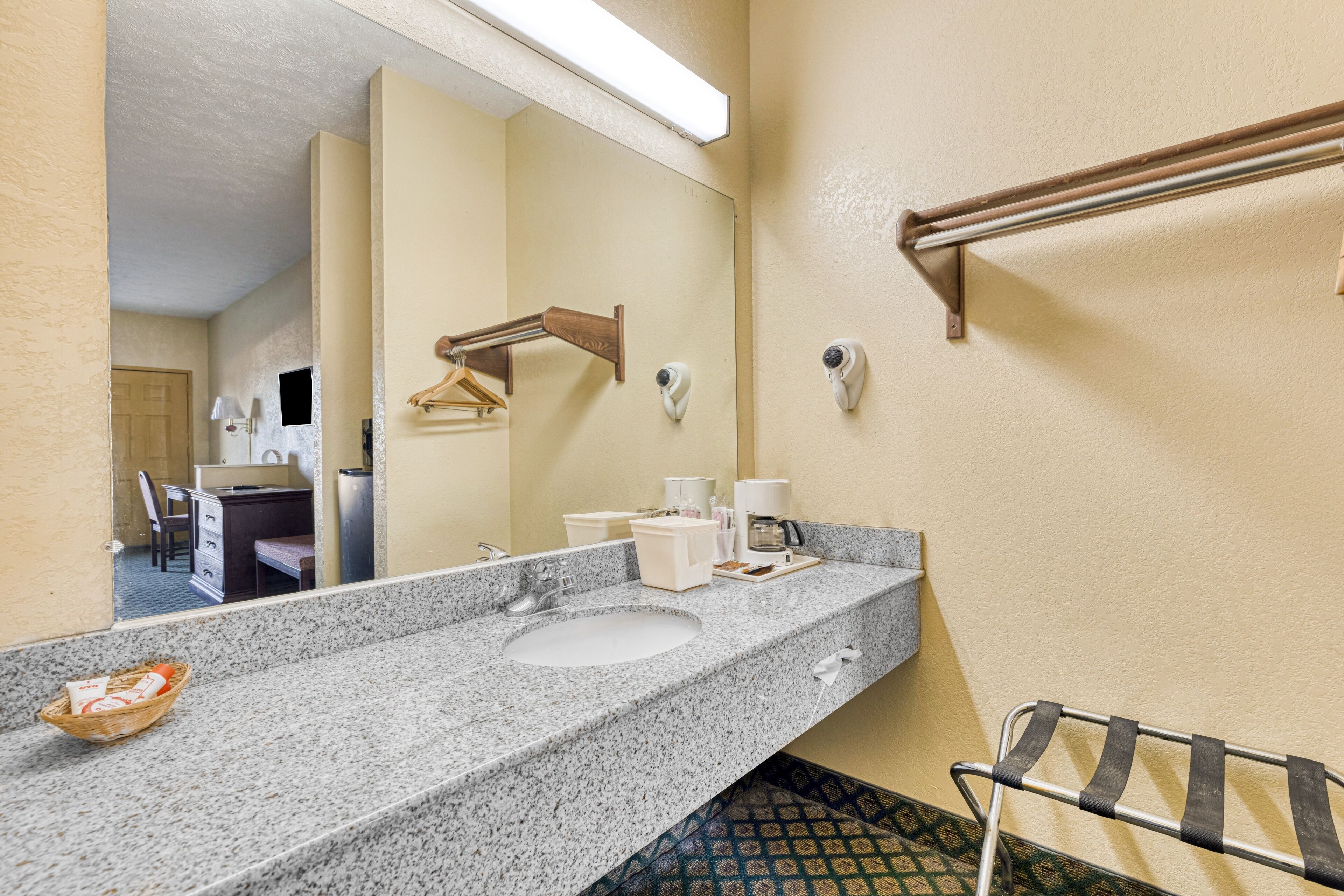 A hotel bathroom with a granite countertop, a sink, a towel rack, and a mirror.