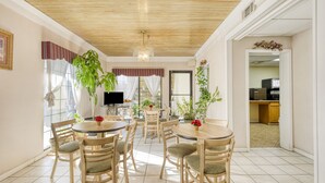 A dining area with wooden tables and chairs, a television, and potted plants.