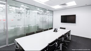 A conference room with a long table, chairs, a phone, and a TV on the wall.