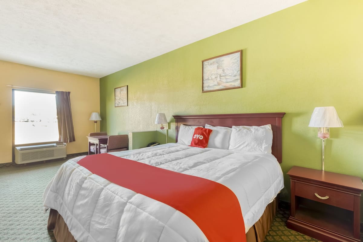 A hotel room with a large bed, a nightstand, a desk, and a window with curtains.