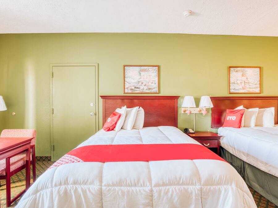 A hotel room with two beds, a desk, and a chair. There are two paintings on the wall.