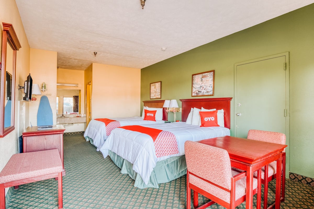 A hotel room with two beds, a desk, and a dining table.