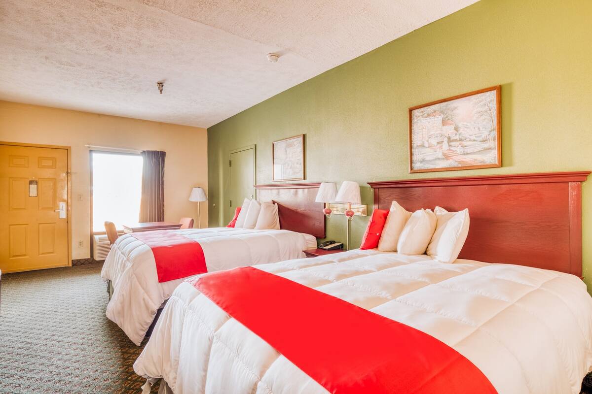 A hotel room with two beds, a wooden headboard, a painting on the wall, and a window with curtains.