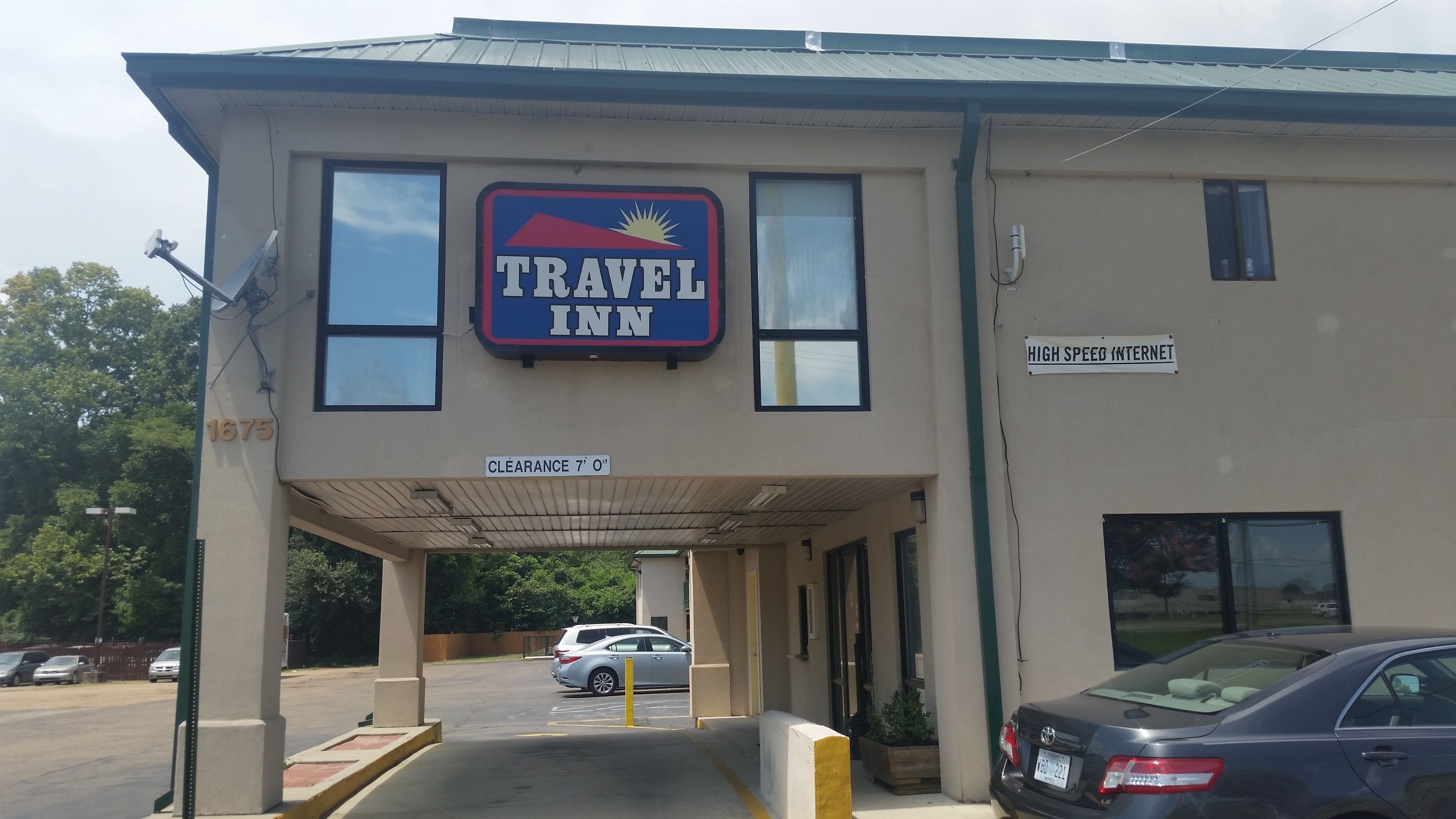 Edificio de Travel Inn con entrada despejada, un cartel que indica internet de alta velocidad y un estacionamiento con coches.