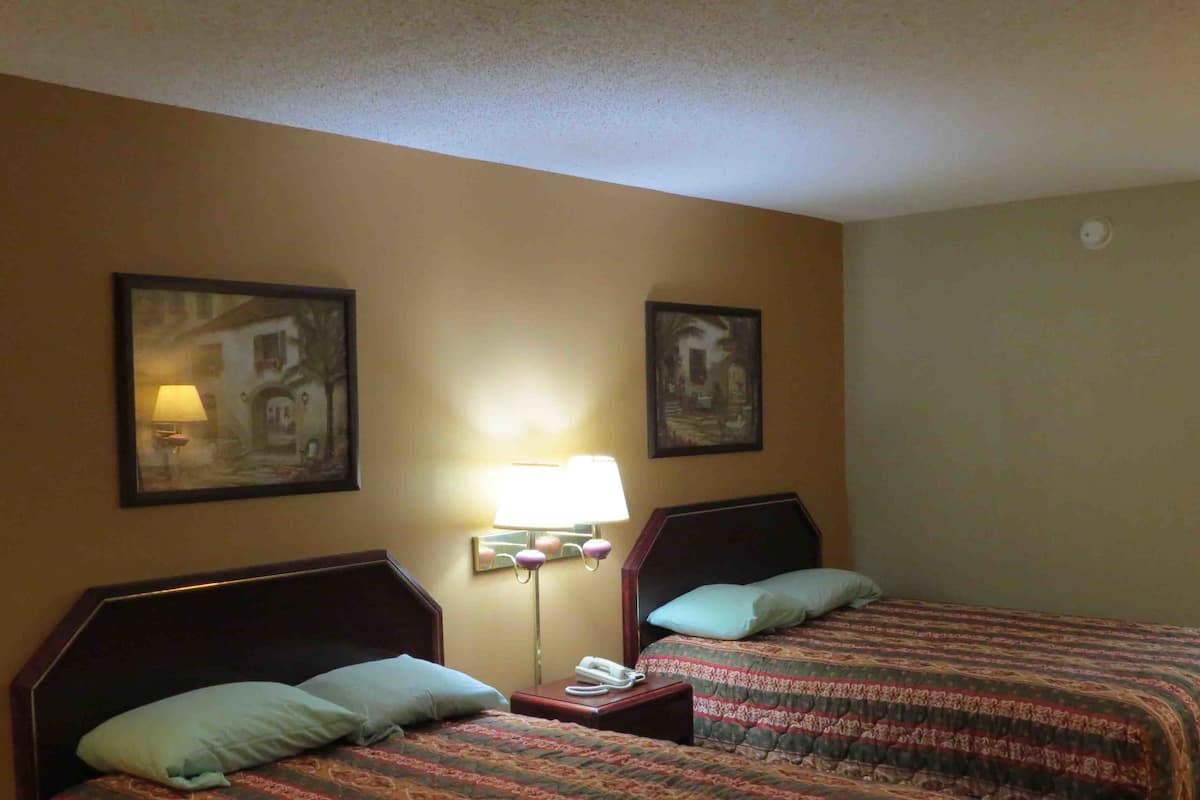 Ein Hotelzimmer mit zwei Betten, jeweils mit Kopfstütze, einem Nachttisch mit Lampe und Telefon. An der Wand hängen zwei gerahmte Bilder.
