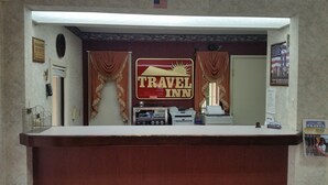 Uma mesa de recepção com uma placa 'Travel Inn', o logotipo da Coca-Cola e uma placa indicando 'Gerente de Plantão'.