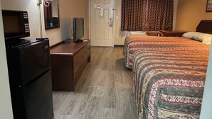 Quarto de hotel com uma cama, uma escrivaninha com televisão, um frigorífico e um candeeiro.