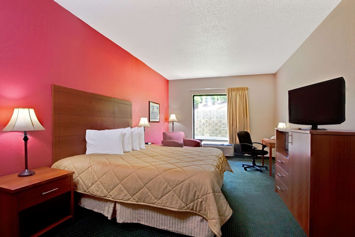 Habitación de hotel con cama, escritorio, silla, televisor y ventana con cortinas.