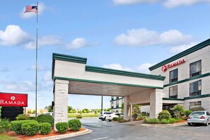 A Ramada hotel with a covered parking area, a flagpole with the American flag, and a signboard.