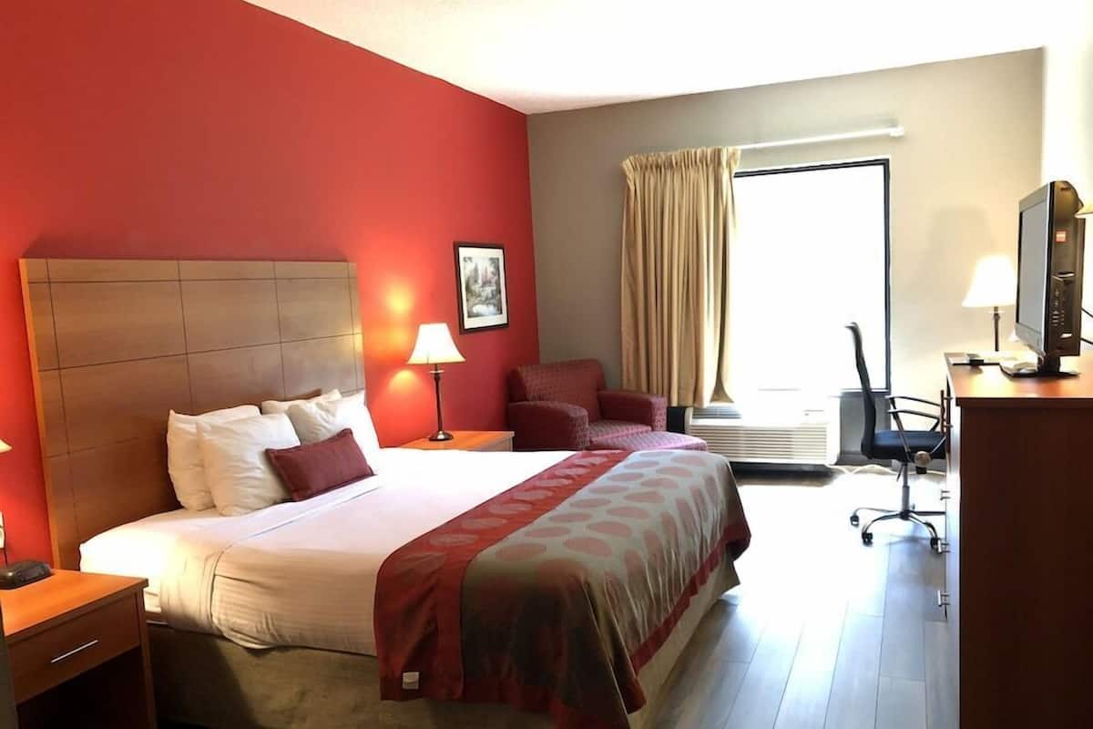 Habitación de hotel con una cama grande, un escritorio con computadora, una silla y un ventanal con cortinas.