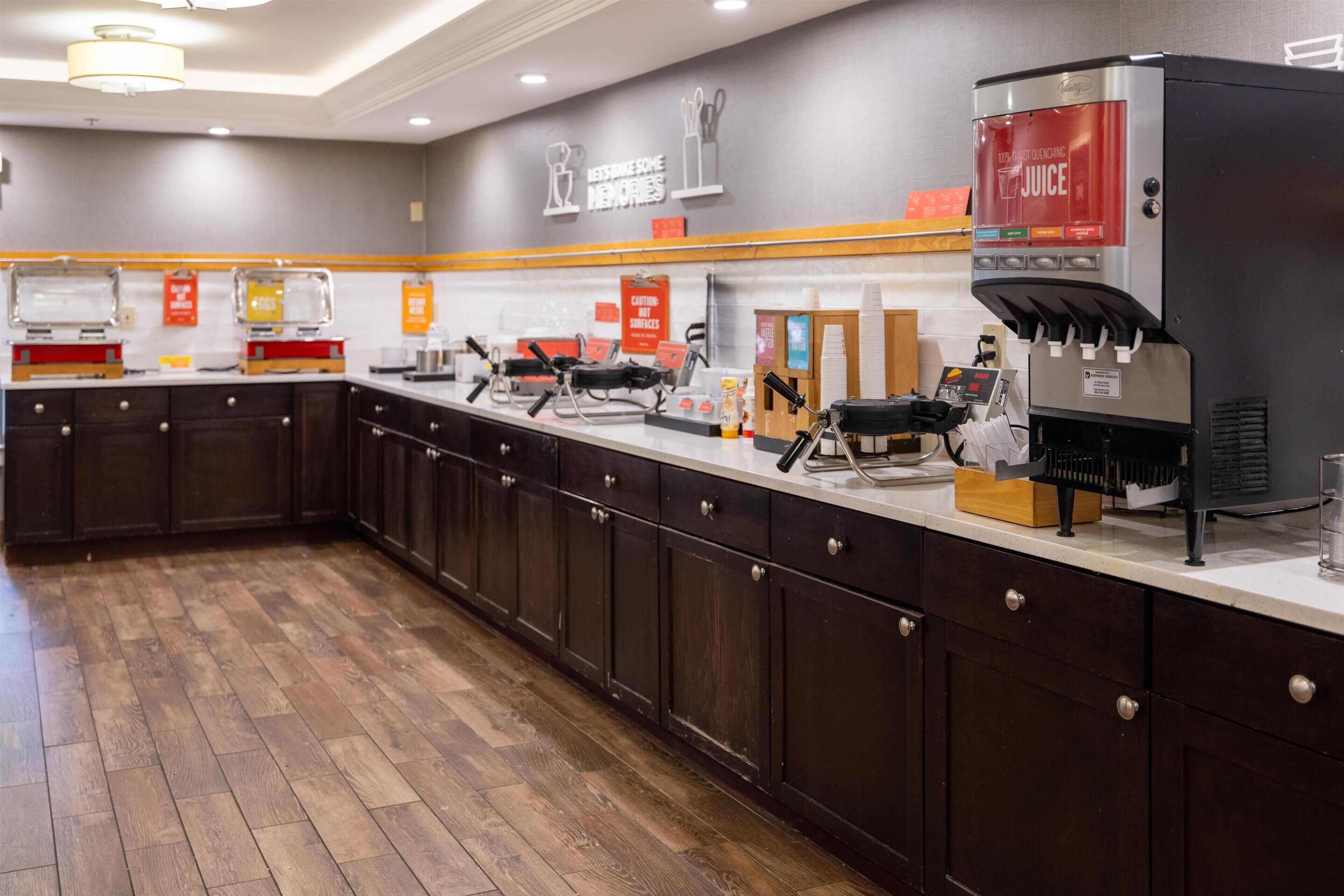 A modern kitchen area with a coffee machine, condiment dispensers, and a sign promoting juice.