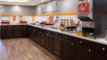 A modern kitchen area with a coffee machine, condiment dispensers, and a sign promoting juice.