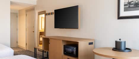 Una habitación de hotel con una cama, un microondas, una mesita con una tetera, un televisor montado en la pared y un cuadro enmarcado.