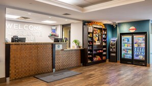 Zona de recepción de un hotel con mostrador de registro, quiosco de auto servicio, bar de aperitivos y exhibición refrigerada de dulces.