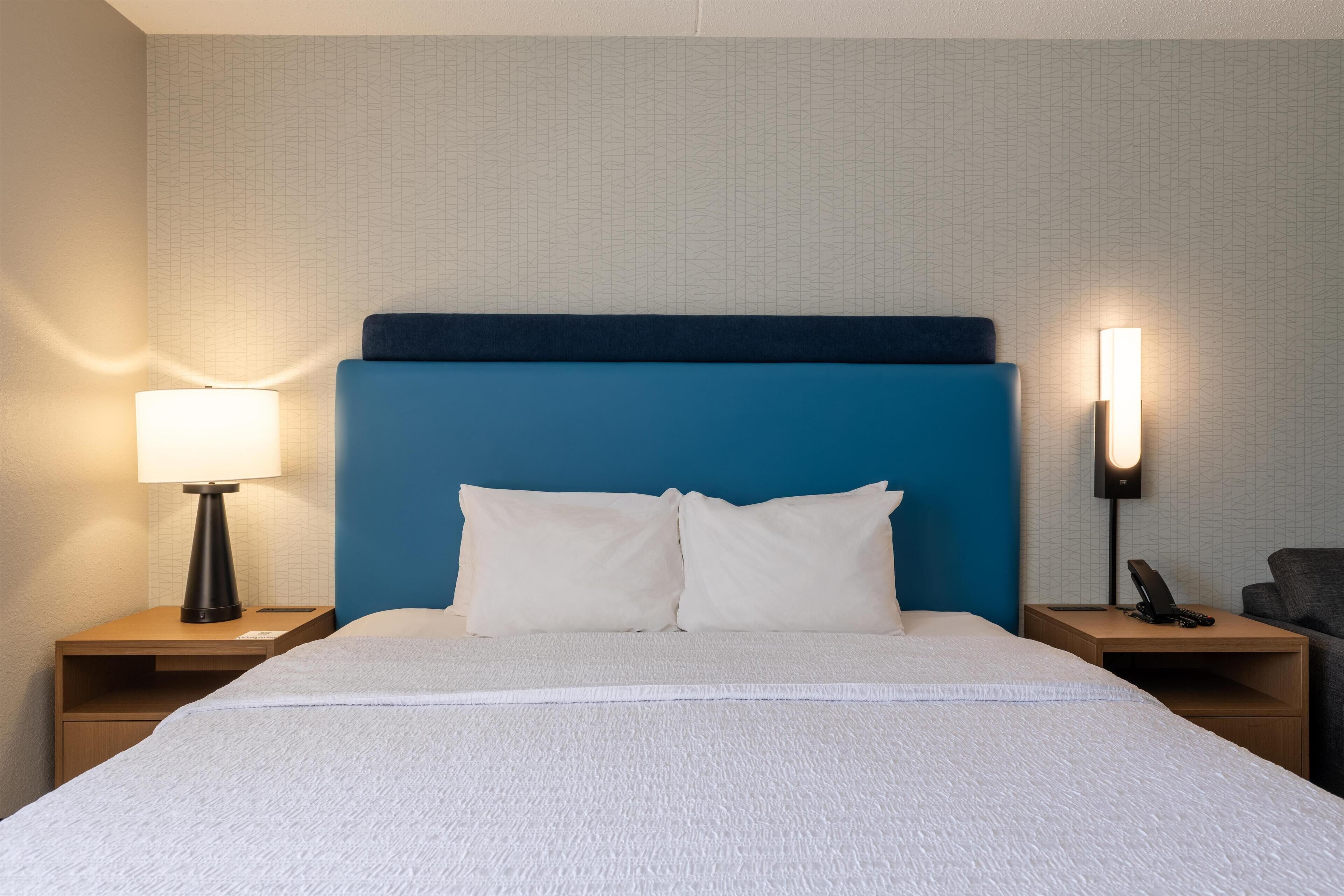 A hotel room with a bed, two bedside tables, a lamp, and a phone on one of the tables.