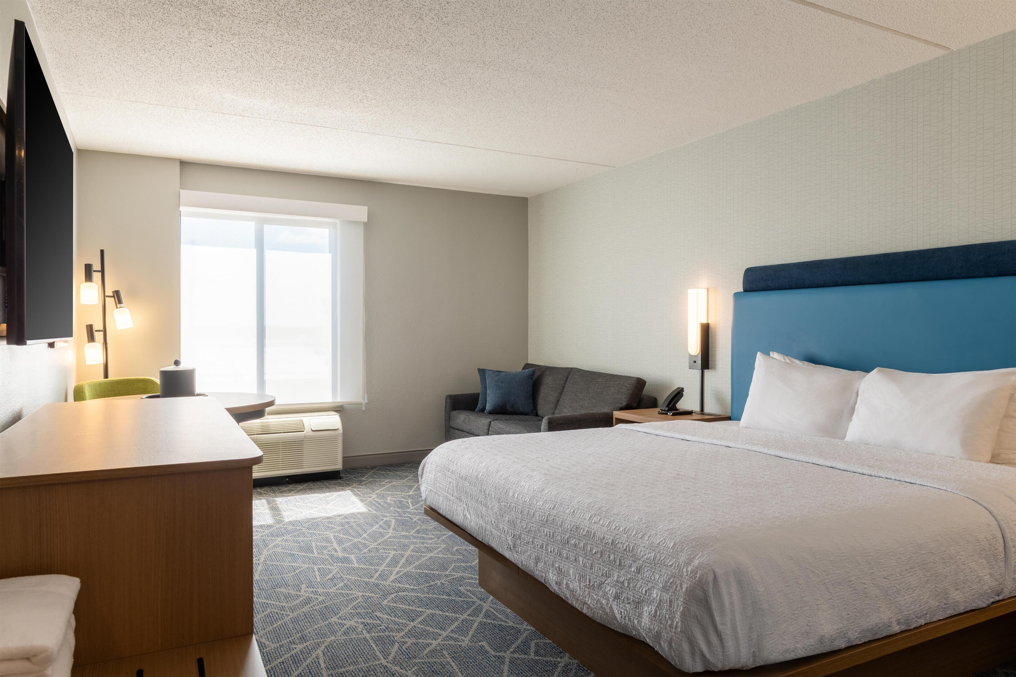 A hotel room with a large bed, a desk, a chair, a sofa, and a window.