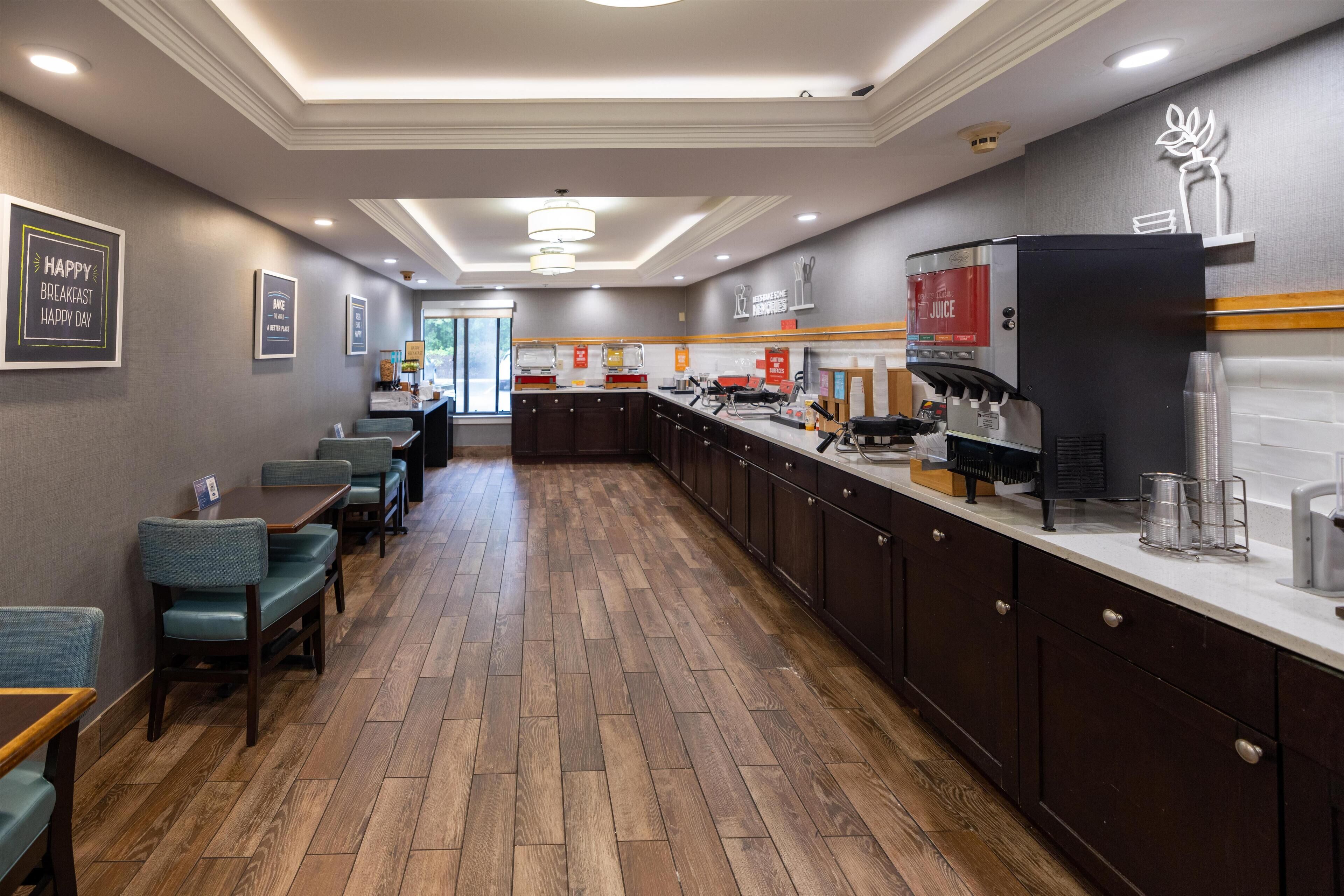 A modern hotel kitchen with wooden flooring, dark cabinetry, and a coffee station.