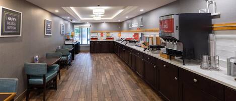A modern hotel kitchen with wooden flooring, dark cabinetry, and a coffee station.