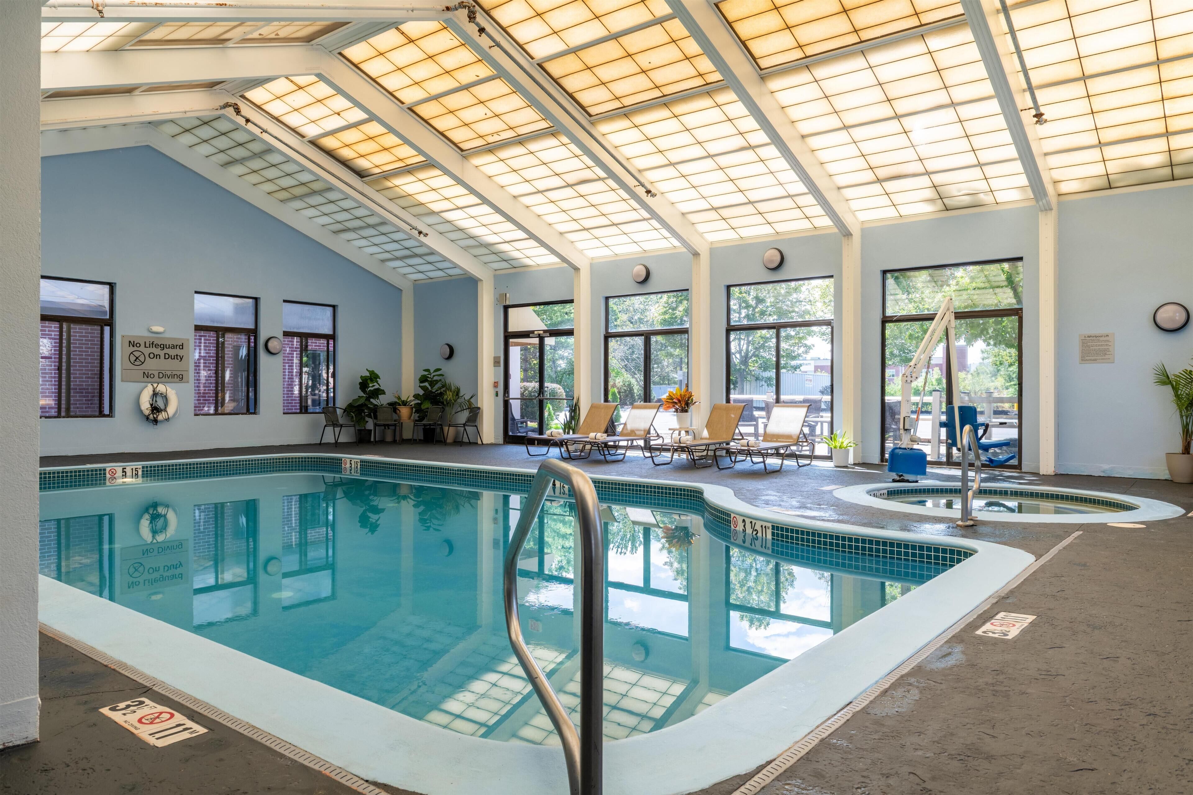 Una piscina interior con suelo de baldosas, una escalera de piscina y un techo con tragaluces.