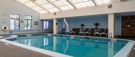 An indoor swimming pool with clear water, a no diving sign, and lounge chairs.