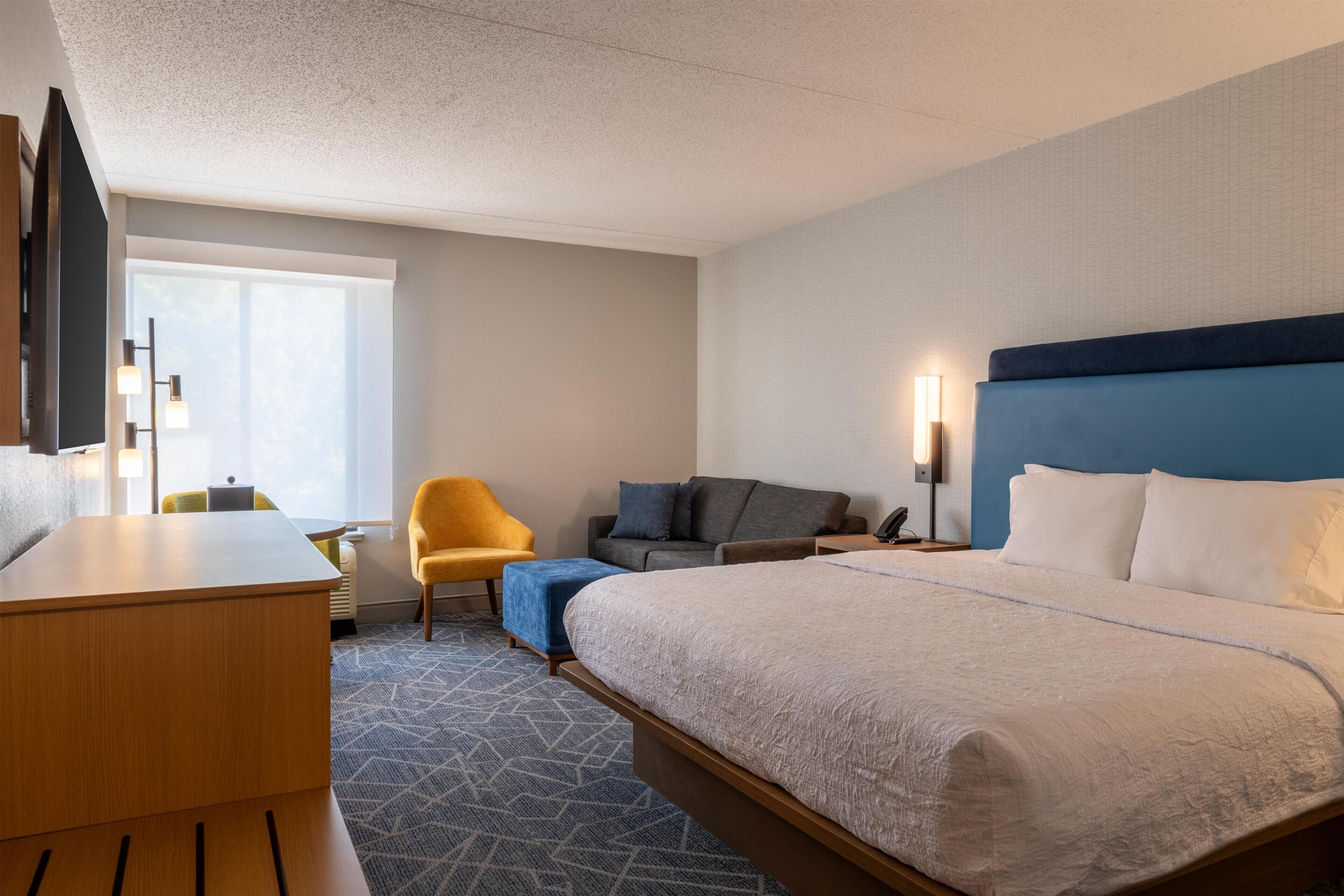 A hotel room with a large bed, a desk, a chair, and a TV.