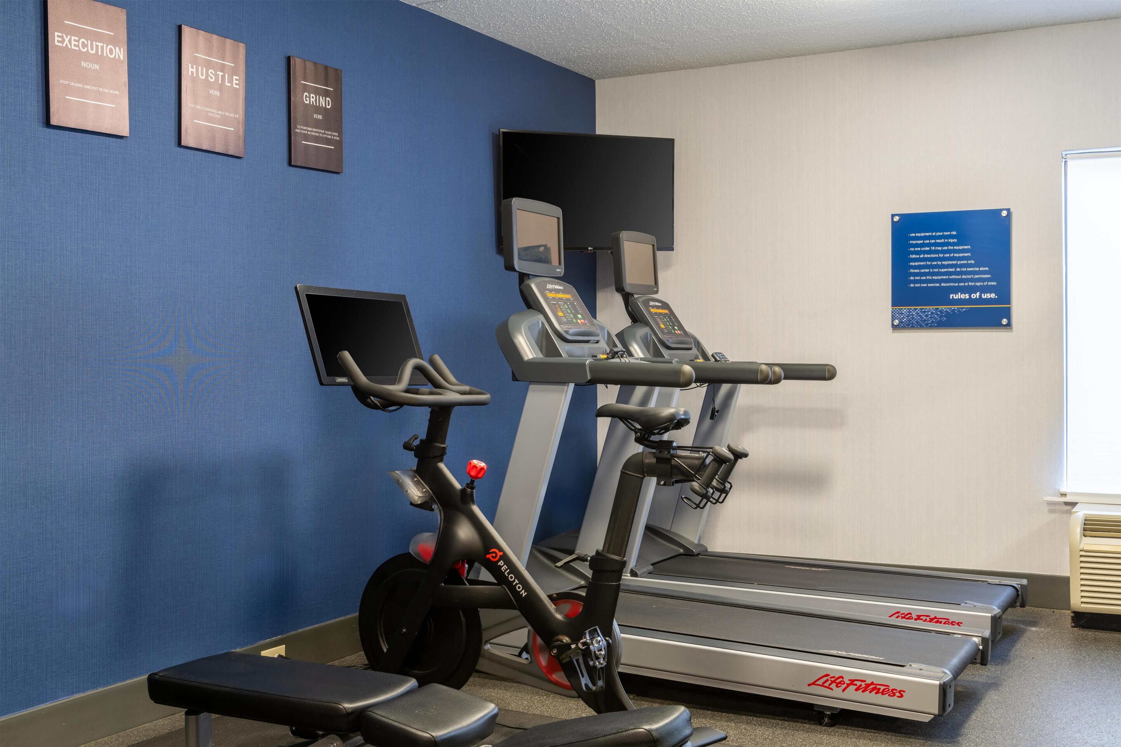 A gym with treadmills, stationary bikes, and a bench. There are motivational posters on the wall.