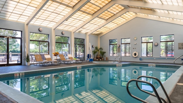 Una piscina interior con techo de tragaluces, sillones de descanso y vistas al exterior.