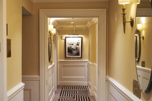 A hallway with a patterned carpet, a framed picture on the wall, and wall sconces.