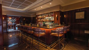 Uma área de bar com teto alto, balcão de madeira e vários bancos.