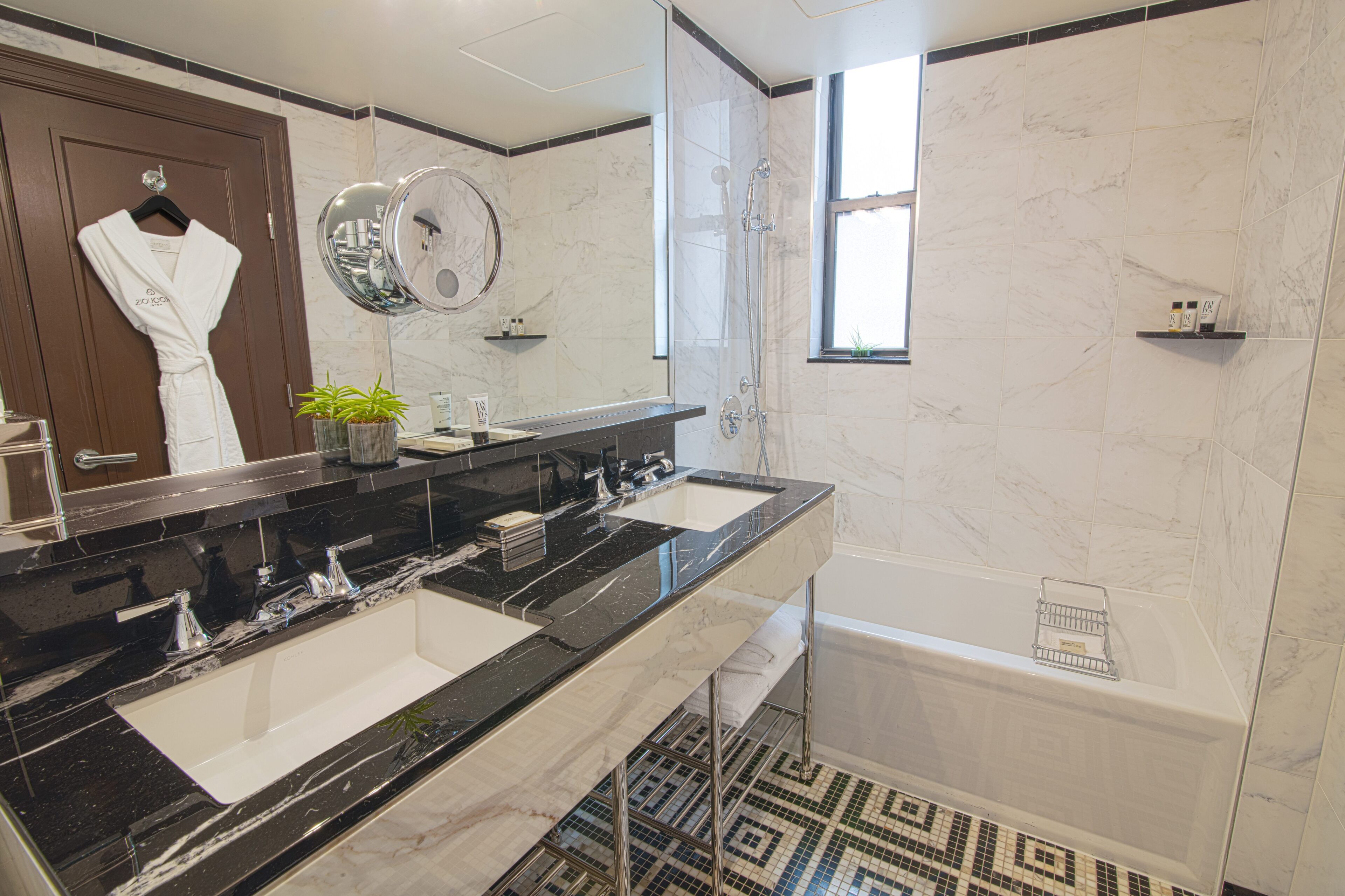 A modern bathroom with two sinks, a bathtub, a large mirror, and a potted plant.