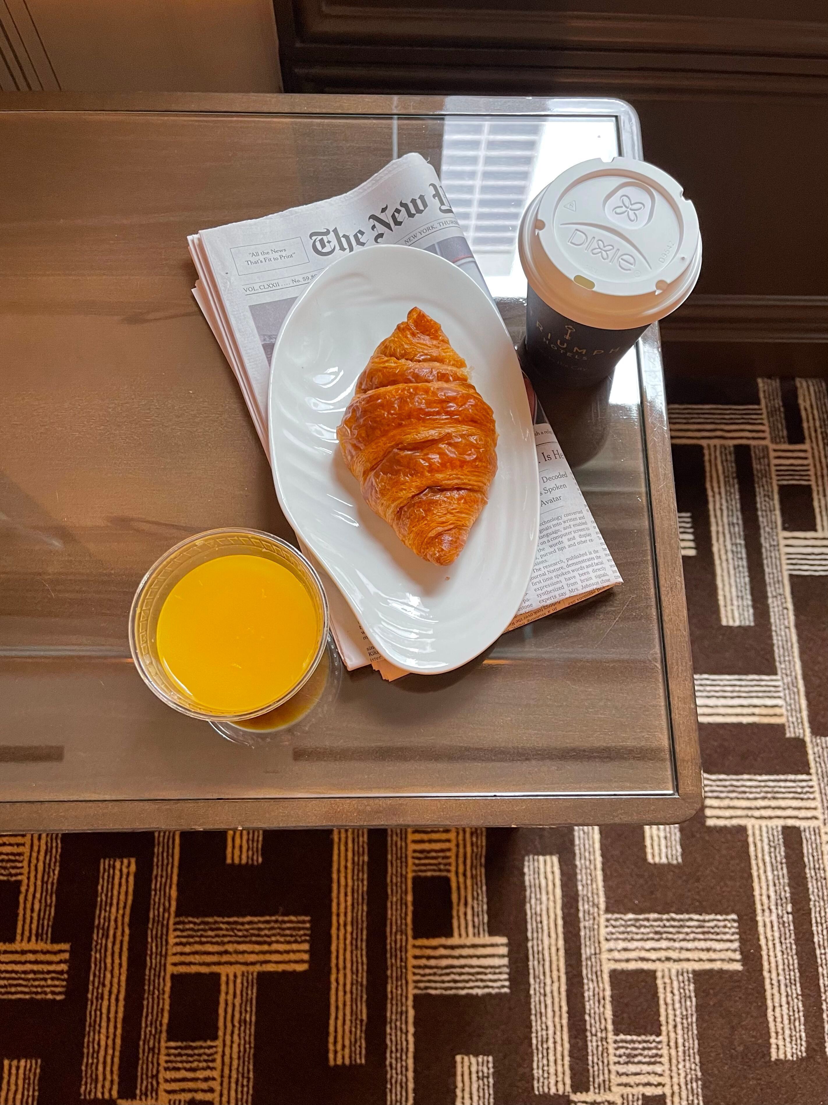 A glass table with a croissant, a cup of coffee, and a glass of orange juice.