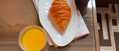 A glass table with a croissant, a cup of coffee, and a glass of orange juice.