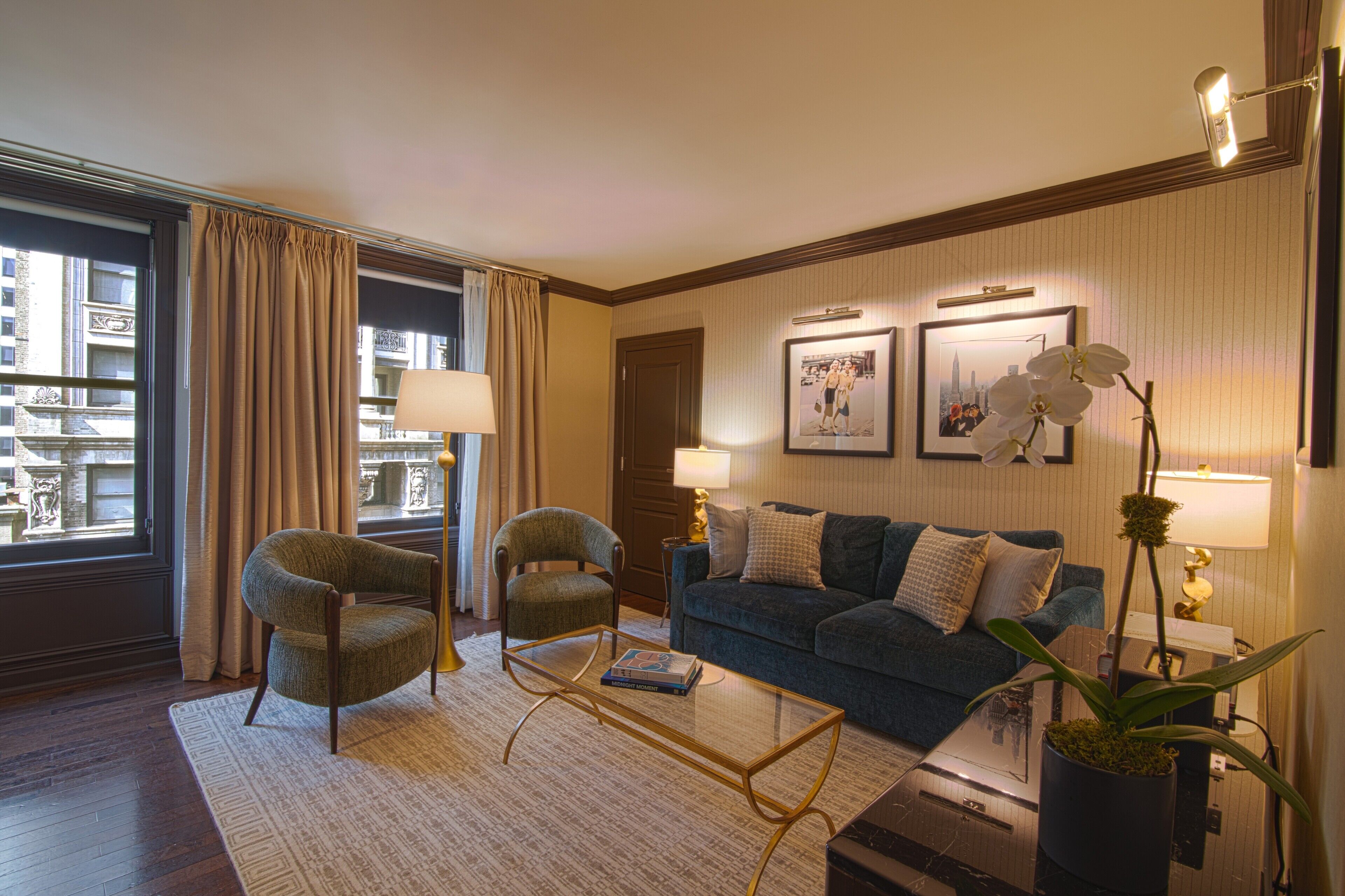 A hotel room with a sofa, two armchairs, a coffee table, a potted plant, and two lamps.